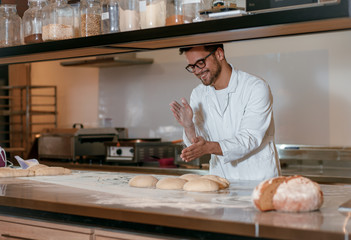 Young male baker preparing dough for bread in modern manufacturing.