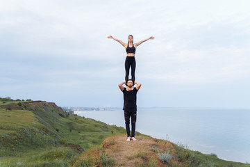 Strong, muscular athlete holding on his shoulders a fit, beautiful sportswoman girl. Acrobats...