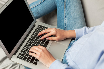 A young girl sits on a couch and holds a laptop with a lap isolated on a black screen. Remote work, distance education and blogging.