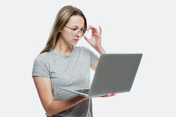 A young girl with glasses holds a laptop in her hands and looks intently at the monitor. Remote work, distance education and blogging. Isolated on a white background.