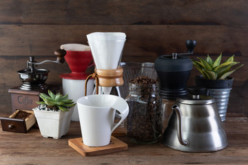 Coffe drip set with,roasted beans,kettle,grinder,white cup and flower pot on wood table and background