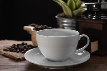 White coffee cup,coffee grinder and roasted beans  in glass jar on wooden table with dark background