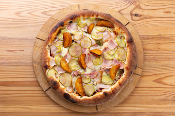 hearty italian pizza on a wooden board. pizza with ham, pickles, bacon and french fries