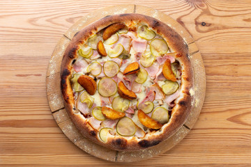 hearty italian pizza on a wooden board. pizza with ham, pickles, bacon and french fries