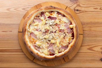 hearty italian pizza on a wooden board. pizza with ham, chicken and pineapple