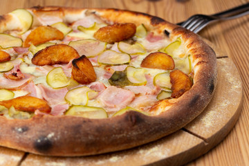 hearty italian pizza on a wooden board. pizza with ham, pickles, bacon and french fries