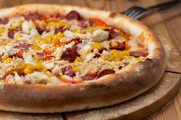 hearty italian pizza on a wooden board. crispy cheese pizza with hunting sausages, pepper, chicken and corn