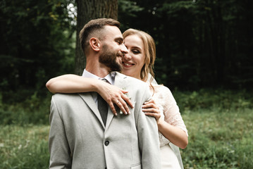 the bride gently hugs the groom from the back and happily whispers in his ear the kind words on the wedding day,Wedding couple. Happy bride with wedding bouquet holds the groom's arm. Stylish 