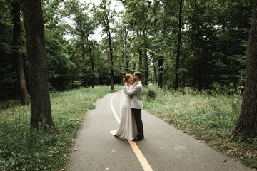 Fototapeta premium the bride gently hugs the groom from the back and happily whispers in his ear the kind words on the wedding day,Wedding couple. Happy bride with wedding bouquet holds the groom's arm. Stylish 