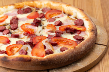 hearty italian pizza on a wooden board. .crispy cheese pizza with hunting sausages, tomato and ham