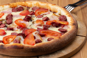 hearty italian pizza on a wooden board. .crispy cheese pizza with hunting sausages, tomato and ham