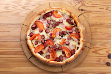 hearty italian pizza on a wooden board. .crispy cheese pizza with hunting sausages, tomato and ham