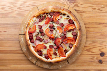 hearty italian pizza on a wooden board. .crispy cheese pizza with hunting sausages, tomato and ham