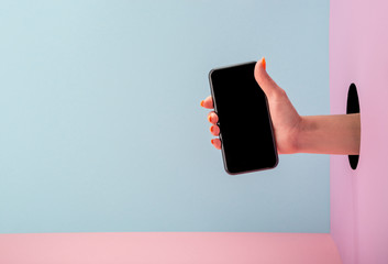 Woman's hand holding a phone on blue and pink background