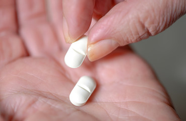 Extreme Nahaufnahme: Zwei weiße Tabletten in der Hand einer älteren Frau, eine Tablette wird...