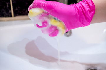A hand in a pink glove washes a washbasin in the bathroom with a sponge with foaming detergent. Cleaning company cleans the house. Disinfection of the senile node from viruses and bacteria.