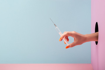 Woman's hand holding a syringe on blue and pink background