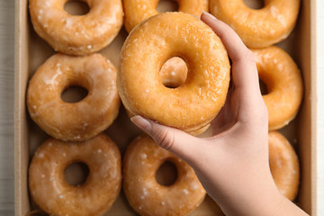 Woman holding delicious donut at white wooden table, top view