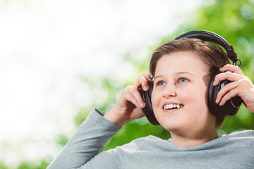 Boy listening a music by huge headphones in outside forest, bokeh background