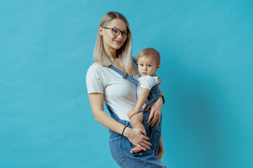 Cheerful young mom posing with her one year kid on blue background