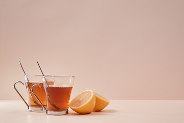 Tea ceremony. Tea time. Two parts of lemon fruit and tea infusion around mugs. Copy space. Isolated on pink background