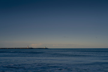 Beach with breakwater and lighthouse visible and calm waves.