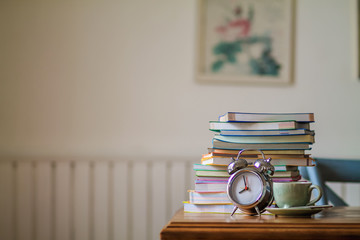 Colorful books and alarm clocks are placed on a wooden table in the house to prepare for online...