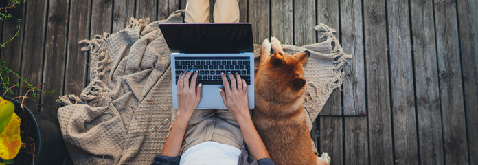 Header for website of young woman sitting on woodern terrace at home with dog using modern laptop...