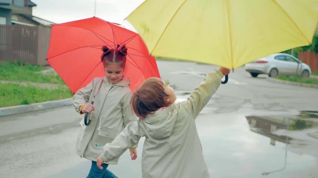 Two sisters are walking along a pool with umbrellas. Red and yellow umbrella. Gray cloak