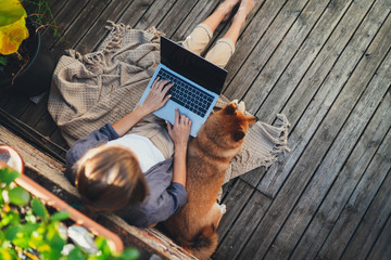 Top-down of young woman working outdoors on home terrace sitting relaxed with dog enjoying sunny...