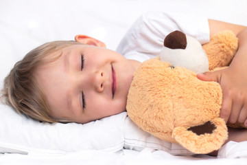Charming little white boy sleeps in bed. hugs a soft toy