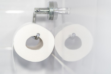 White roll of soft toilet paper neatly hanging on a modern chrome holder. Reflected in the bathroom tiles