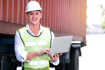 Engineer worker or technical standing in the container yard shipping area and used a laptop or computer to control loading containers into the truck. Industrial and import-export concept
