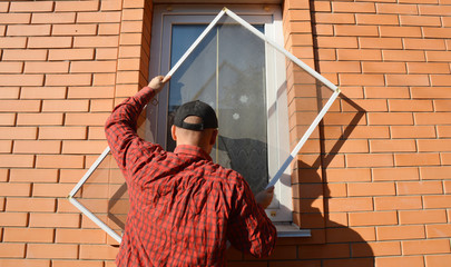 A handyman is installing anti-insect mosquito net, screen, fly and bugs protection on a plastic...