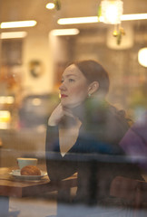 Beauty adult dreaming young woman looking through window at the coffee house restaurant