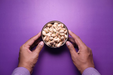 man hand holding a bowl salted pistachios nut on purple background 