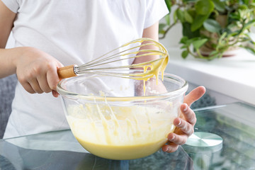 A close-up of the upper body of a child stirs the wafer dough by hand. Stir a delicious dough of flour, eggs, milk and sugar with a whisk. The dough is ready to cook. Children's cook.