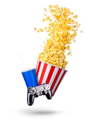 Paper bucket with popcorn, cup of drink and video game joystick on white