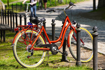 A bright red Bicycle stands at the fence in a green Park on a Sunny day. Moving by bike every day. bicycle at street parking outdoors. use of eco-friendly and sports transport in the city to move