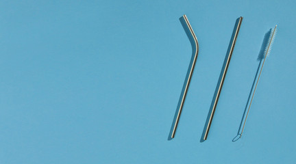 A set of reusable accessories for drinks. A set of steel straws and a cleaning brush. Blue background, top view. The zero waste concept. Copy space.