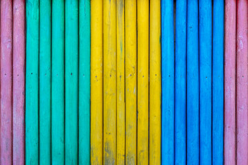 Colorful wooden fence painted in cyan, yellow, blue and purple colors. Multicolored striped texture background.