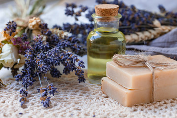 Concept of natural ingredients in cosmetology for gentle skin care. Organic oil in glass bottle, handmade soap bar, brush, dry lavender. Atmosphere of serenity and relax. Rustic wooden background