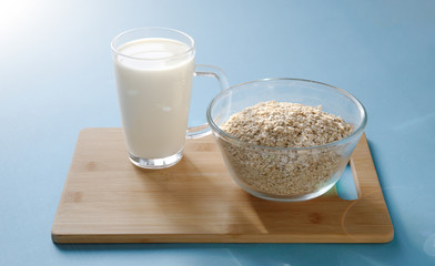 glass of milk and a glass bowl with oatmeal on a wooden board and a blue background