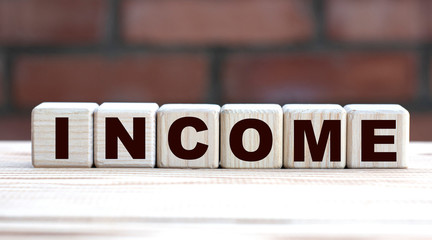 concept word INCOME on cubes against the background of a brick wall