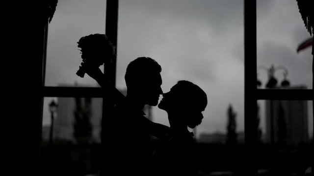Silhouette of a young couple of the bride and groom kiss on the background of the window. Wedding and newlyweds.