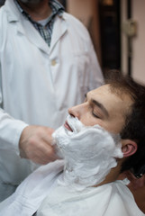 Young and handsome man at a barbershop shaving