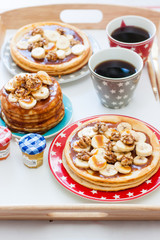 Breakfast tray with pancakes with bananas, maple syrup and nuts, cup of coffee and honey.