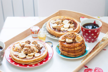 Breakfast tray with pancakes with bananas, maple syrup and nuts, cup of coffee and honey.