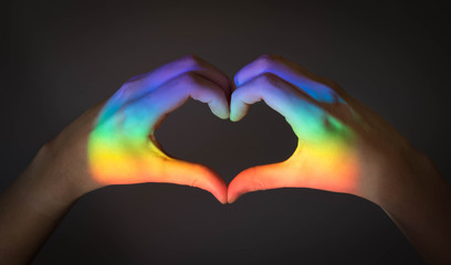 Hands making a heart sign with the colors of the lgbt rainbow flag, symbolizing gay or lesbian love.