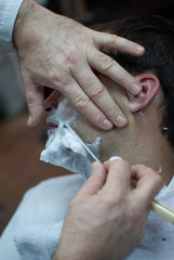 Young man shaving beard with razor in a barbershop